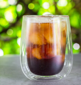 Cold-brew coffee with orange juice and ice on green bokeh background